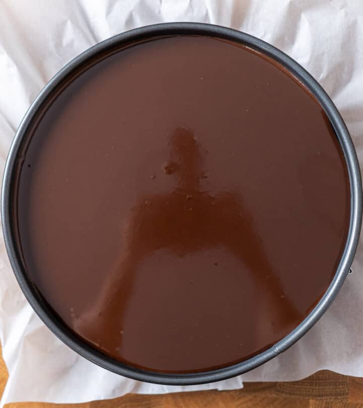 Pouring glossy chocolate ganache over chilled no bake peanut butter chocolate cheesecake