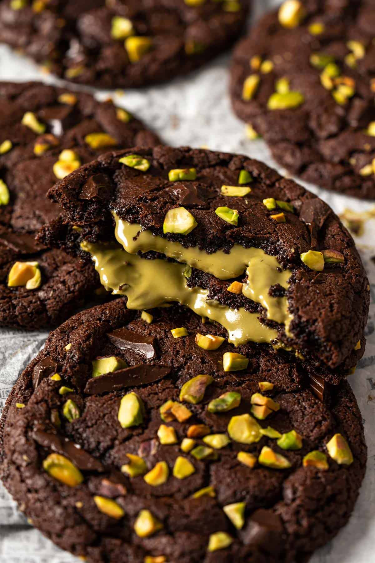 Chocolate pistachio cookie broken open with gooey pistachio cream filling and fudgy brownie-style texture.