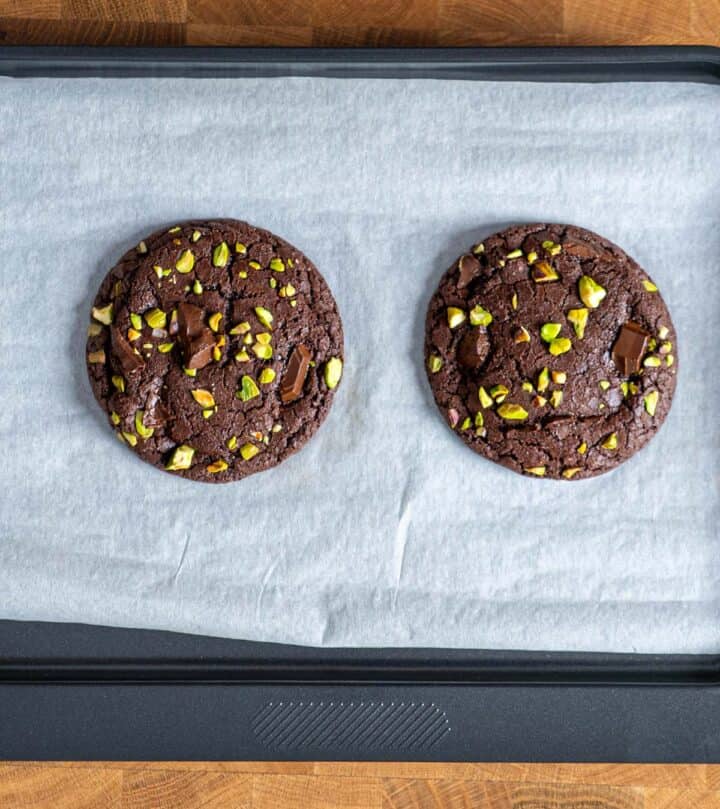Freshly baked chocolate pistachio cookies cooling on tray with shiny ripples.