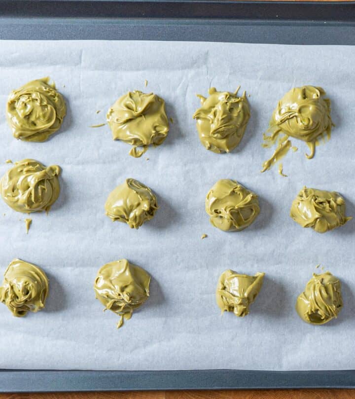 Scooped pistachio cream mounds on tray, ready to freeze for chocolate pistachio cookies.