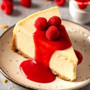 Creamy baked New York cheesecake with no water bath topped with raspberry coulis and fresh raspberries.
