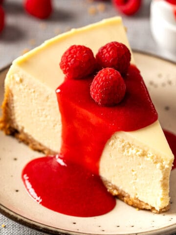 Creamy baked New York cheesecake with no water bath topped with raspberry coulis and fresh raspberries.