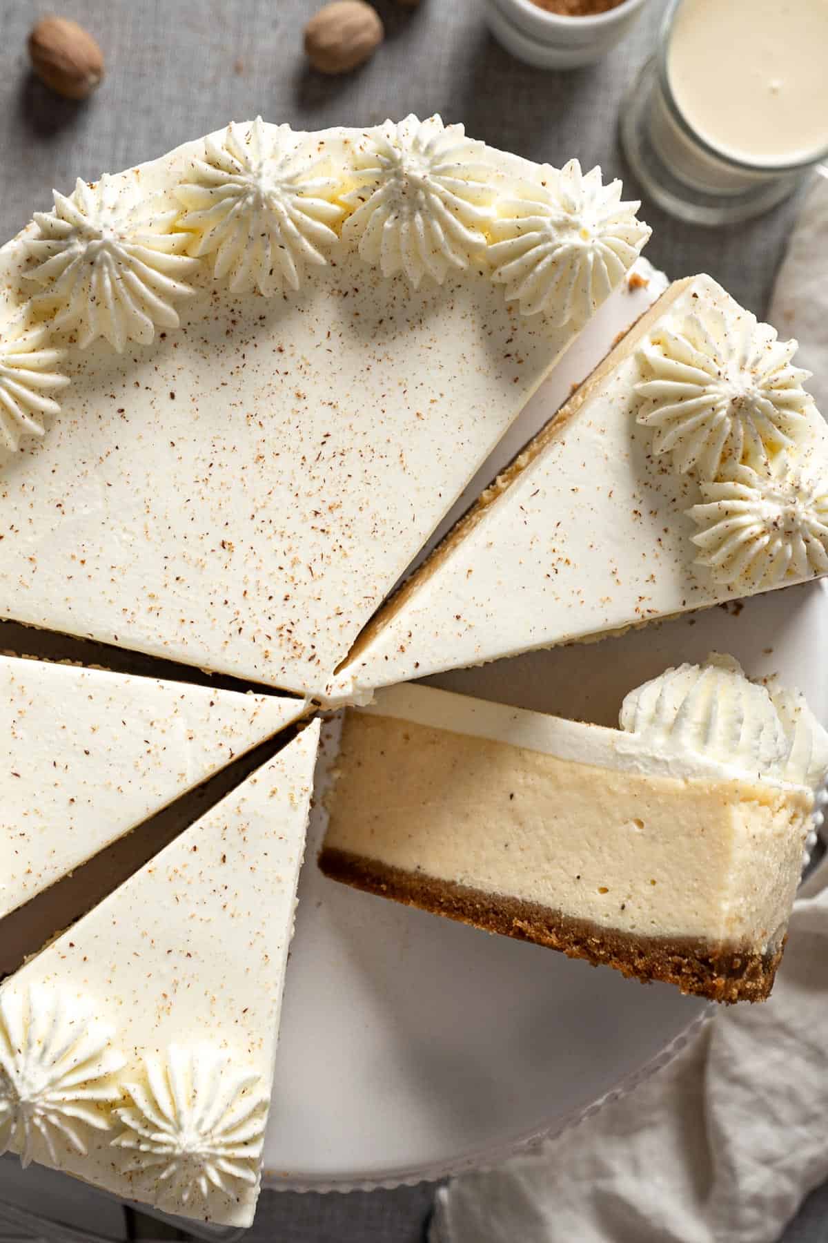 A whole eggnog cheesecake sliced on a cake stand with one piece flipped on the side.