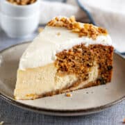 A slice of carrot cake cheesecake with cream cheese frosting on a plate.