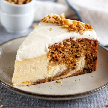 A slice of carrot cake cheesecake with cream cheese frosting on a plate.