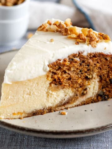 A slice of carrot cake cheesecake with cream cheese frosting on a plate.